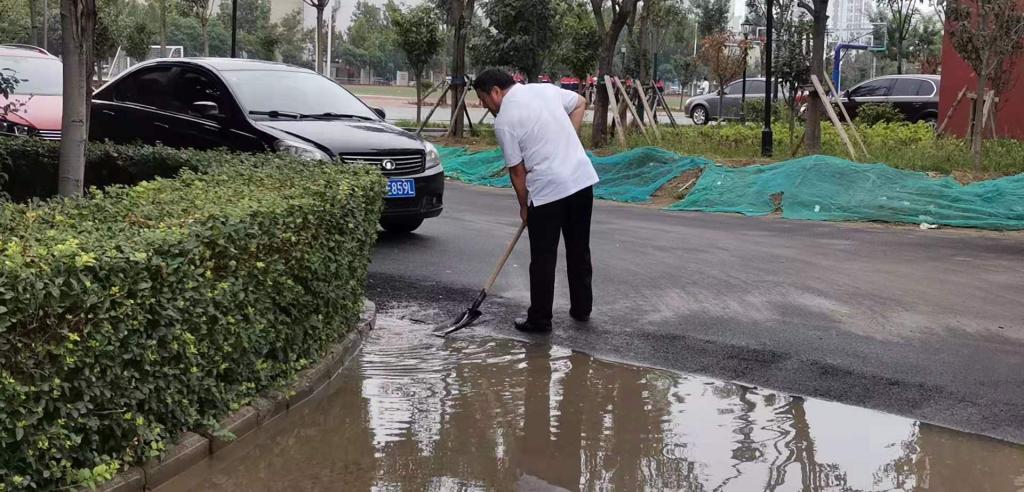 雨后,路面积了一片水坑,常校长拿起铁锹开始排水